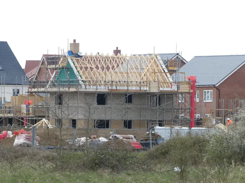 Maison en construction sous échafaudage, avec sa charpente en fermettes de bois encore à nu