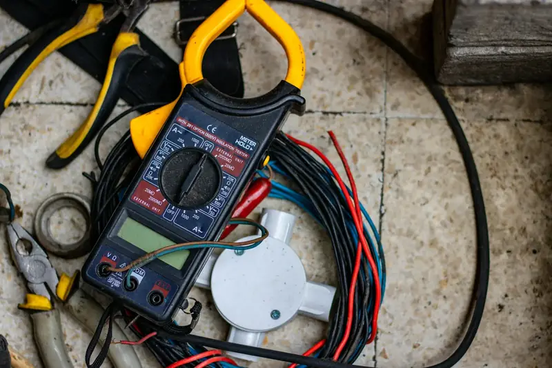 Pince multimètre, câbles électriques et outils d’électricien posés sur un sol de chantier