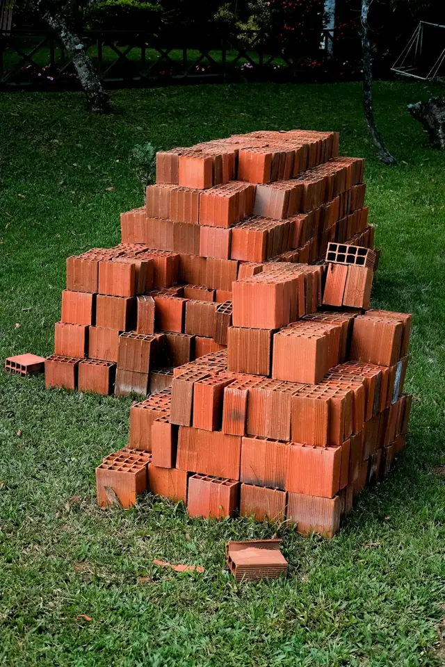 Tas de briques creuses orange posé sur l’herbe, avant le montage d’un mur