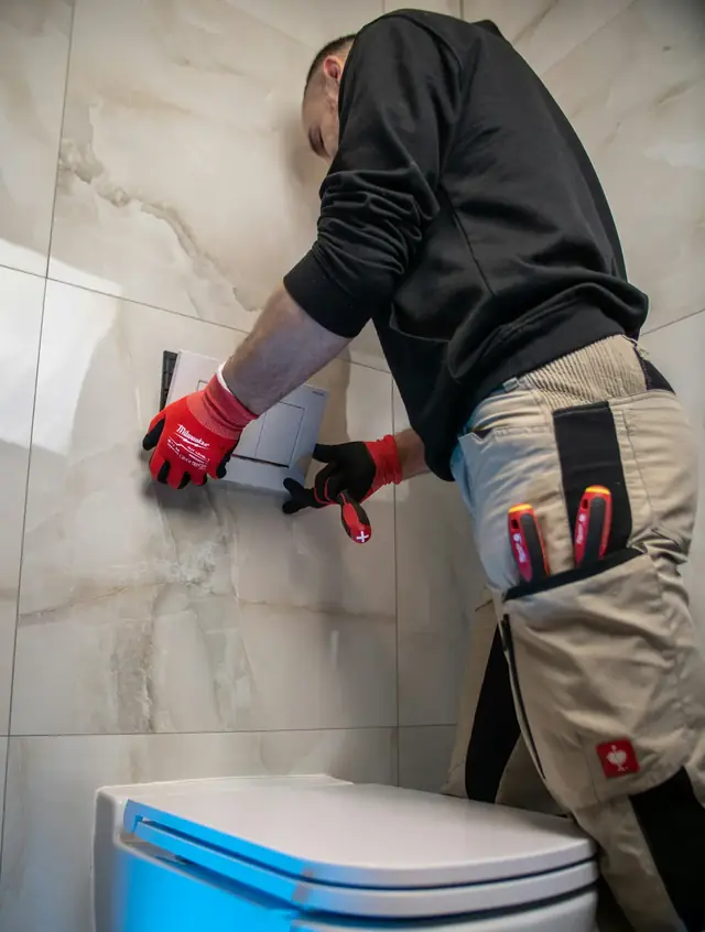 Artisan vu de dos qui perce un mur carrelé de salle de bains au-dessus des toilettes