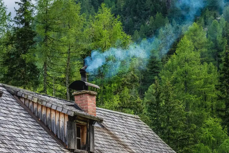 Cheminée qui fume au-dessus d’un vieux toit, avec une forêt de sapins en arrière-plan