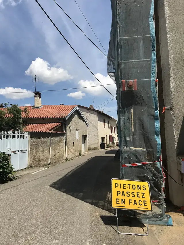Échafaudage bâché le long d’une maison de village pendant un ravalement, dans une rue ensoleillée