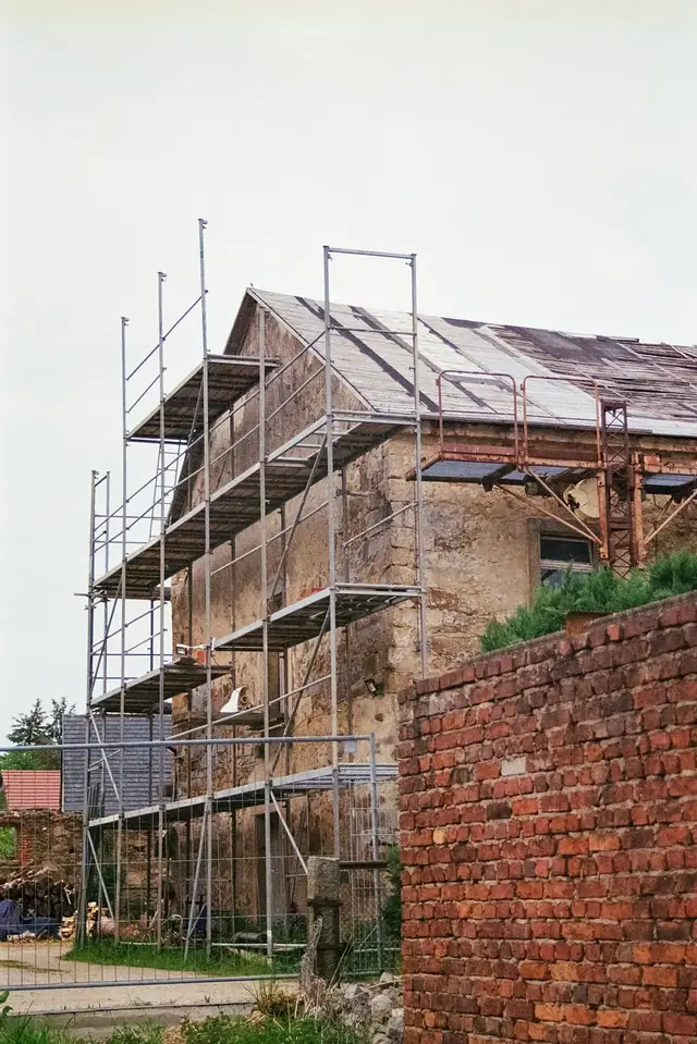 Bâtiment en pierre entouré d’un échafaudage à plusieurs niveaux, filet de protection en pied