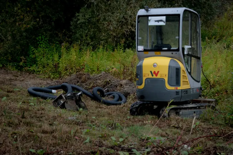 Mini-pelle arrêtée dans une friche, à côté d’une tranchée et de gaines noires