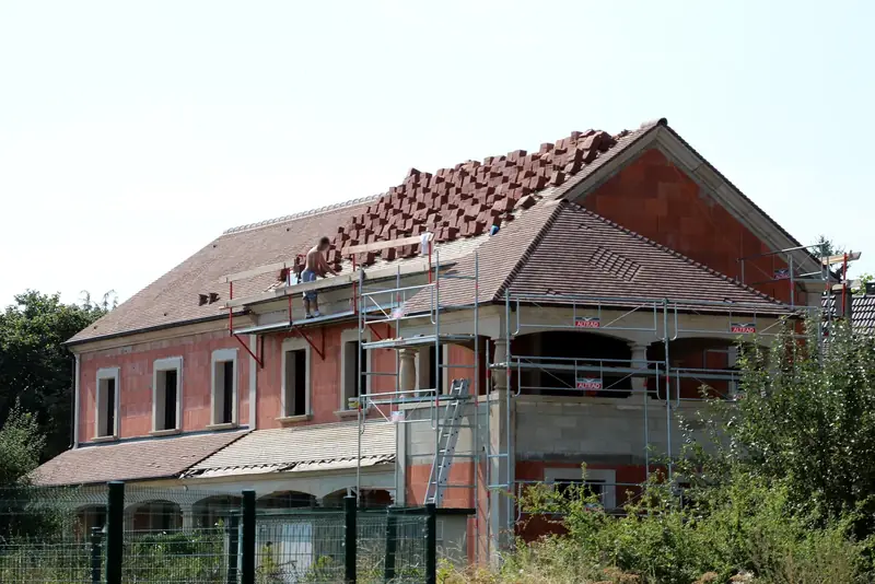 Chantier de couverture : tuiles neuves montées sur le toit d’une maison sous échafaudage