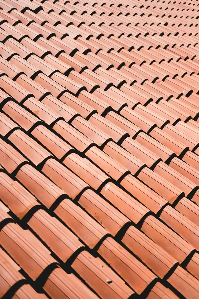 Rangs réguliers de tuiles rouge orangé vus en diagonale, sous une lumière douce