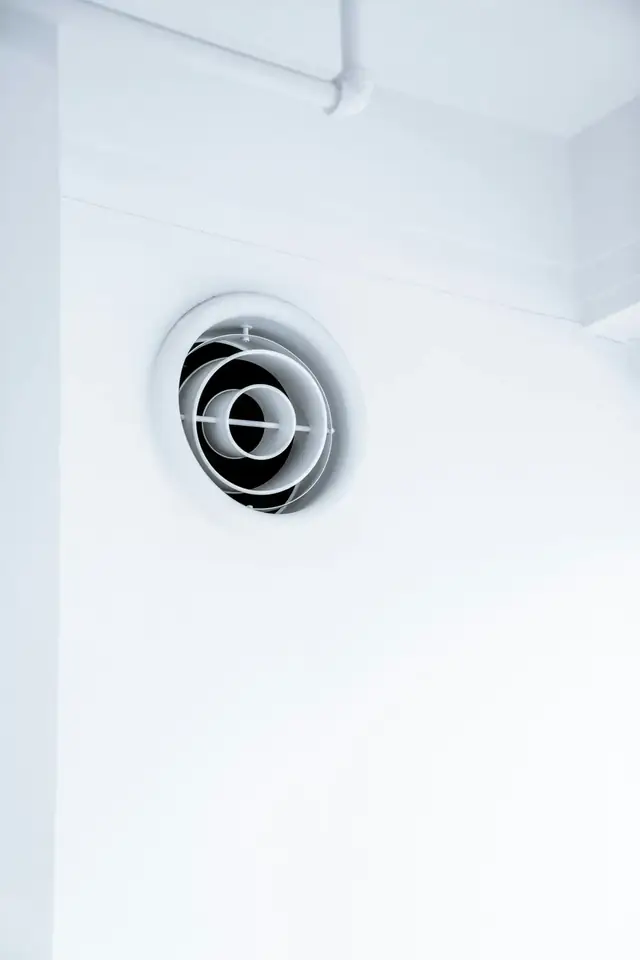 Bouche d’extraction d’air ronde et blanche fixée sur un mur blanc lisse